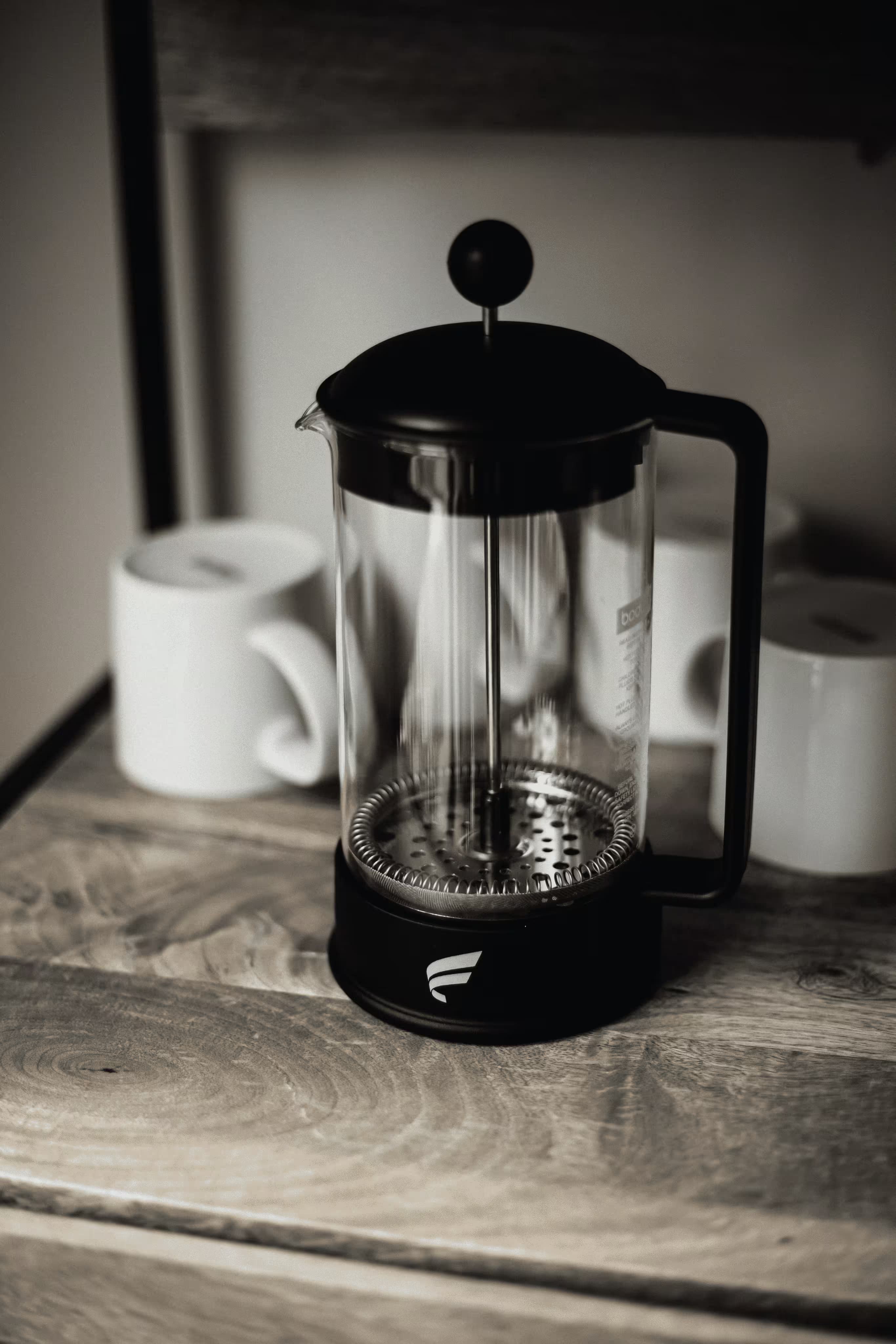 French press with ceramic mugs on wooden surface