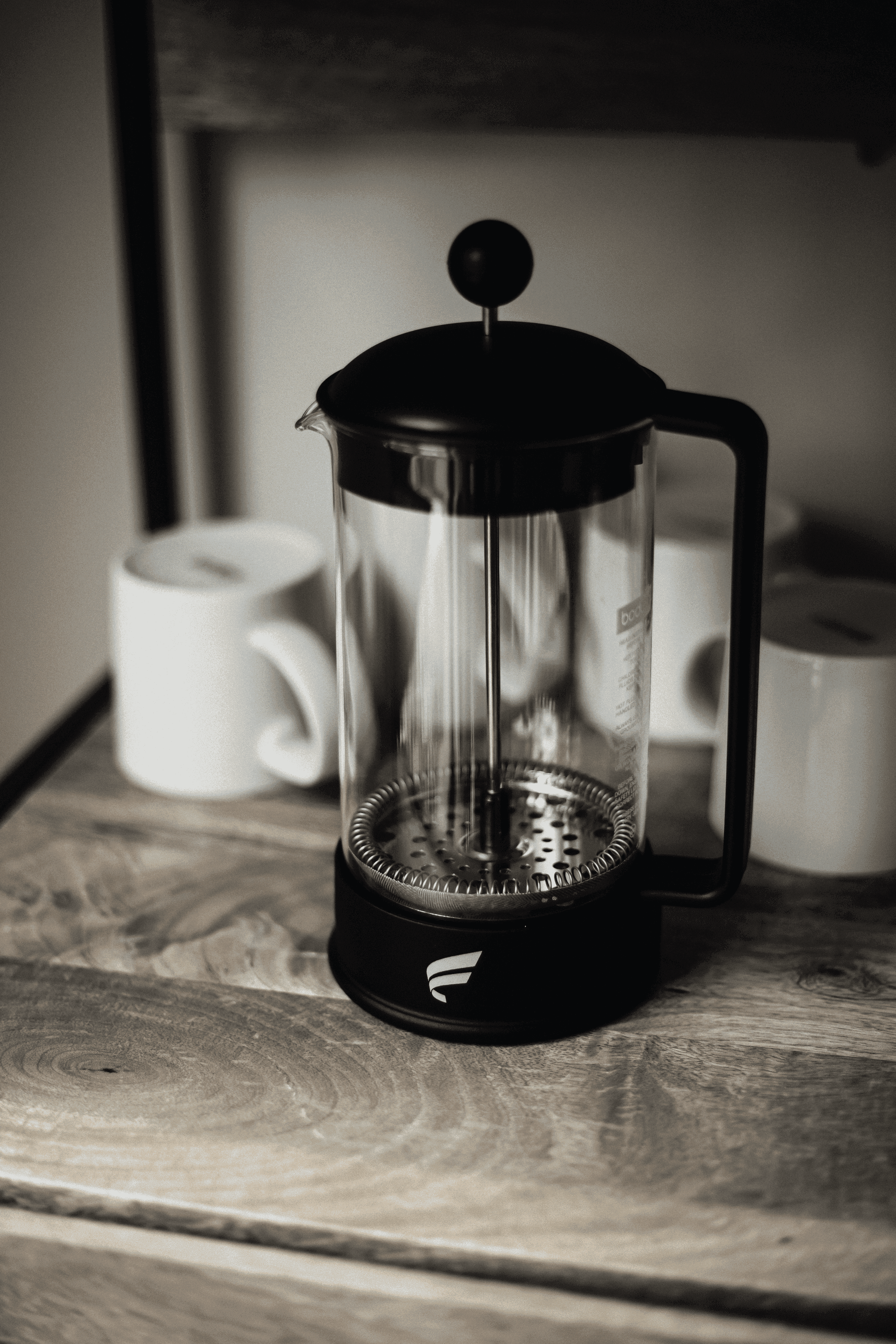 French press with ceramic mugs on wooden surface